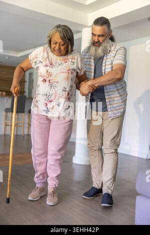 Donna anziana e uomo che cammina a casa, donna in camicetta floreale con sudori rosa che reggono il bastone di legno Foto Stock