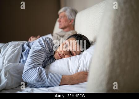 Sconvolta moglie anziana offesa evitando il contatto con il marito mentre si sdraia insieme a letto in camera da letto. Foto Stock