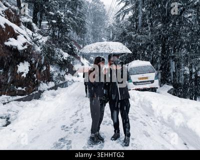 Una coppia ama trascorrere una giornata invernale camminando insieme sotto un ombrello su una strada innevata tra fiocchi di neve cadenti a Dalhousie, Himachal Pradesh, Indi Foto Stock