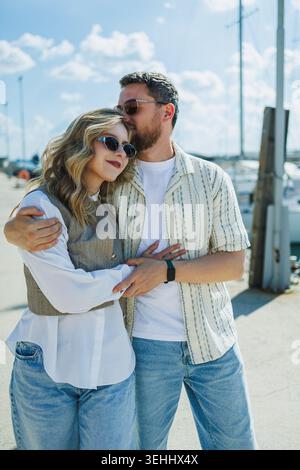 Una coppia si trova vicino a un porticciolo, condividendo un momento di affetto. Sono circondate da barche e dalla luce del sole, godendosi il loro tempo all'aperto Foto Stock