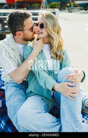 Due persone siedono vicino a una coperta in un ambiente luminoso all'aperto. Condividono sorrisi e risate mentre si godono la compagnia reciproca al sole. Foto Stock