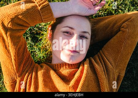Donna che si rilassa sdraiata sull'erba sotto la calda luce del sole Foto Stock