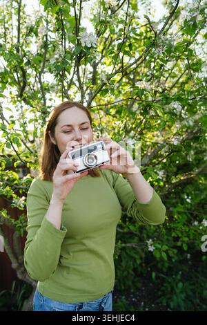 Donna sorridente che scatta foto nel giardino fiorito di primavera Foto Stock
