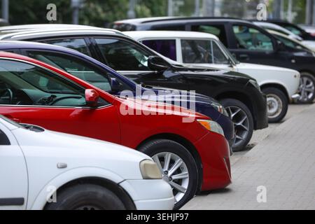 Vista laterale di varie auto moderne parcheggiate in una fila stretta lungo il marciapiede di una strada della città. Concentrati su una berlina rossa brillante. Immagine concettuale per la pa urbana Foto Stock