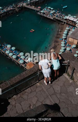 Vista rialzata di una spiaggia affollata con acqua turchese, ombrelloni e piattaforme in legno, destinazione estiva per le vacanze a Sorrento, Italia. Foto Stock