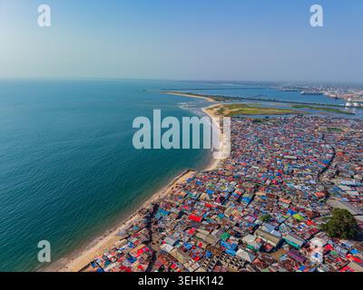 Vista aerea dei tetti colorati e densamente pieni di un insediamento costiero lungo una spiaggia sabbiosa e l'Oceano Atlantico blu a Monrovia, Liberia. Foto Stock