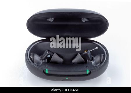 Due auricolari wireless neri si trovano all'interno di una custodia di ricarica nera aperta su uno sfondo bianco. Sul caso sono visibili tre luci verdi. Foto Stock