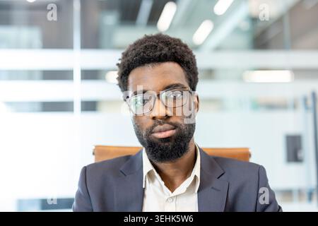 Uomo d'affari professionista con barba e occhiali seduti in ufficio. Un'espressione seria e mirata. Riflettere fiducia e una forte etica lavorativa in un ambiente aziendale Foto Stock