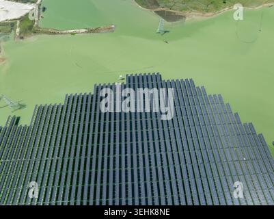 Vista aerea di un grande pannello solare galleggiante sull'acqua verde con piloni elettrici e paesaggio rurale di Sirajganj, Rajshahi Division, Bangladesh. Foto Stock