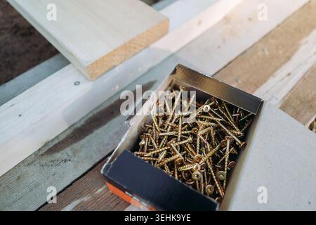 Una scatola di viti da costruzione poggia su una tavola di legno di larice preparata per l'assemblaggio di un'aiuola rialzata alta. Vista dall'alto Foto Stock