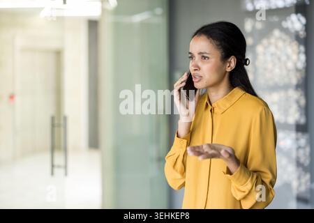 Donna che si sente stressata e frustrata mentre parla al telefono cellulare, ha una conversazione seria tra le sfide sul posto di lavoro e la pressione emotiva Foto Stock