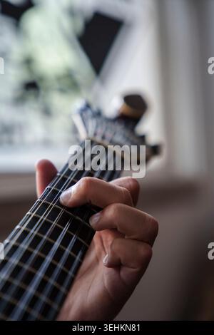 Primo piano di una mano che suona un accordo su una tradizionale tastiera per chitarra portoghese con una profondità di campo bassa Foto Stock