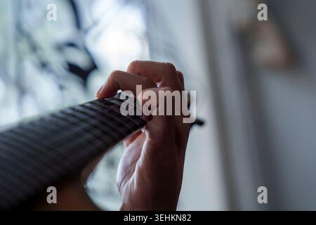 Primo piano della mano di una persona che suona un accordo su una tastiera di chitarra con un morbido sfondo sfocato Foto Stock