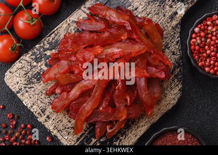 Cibo, fette di pollo essiccate, con gusto di ciliegia o prugna, sale e spezie su sfondo di cemento scuro Foto Stock