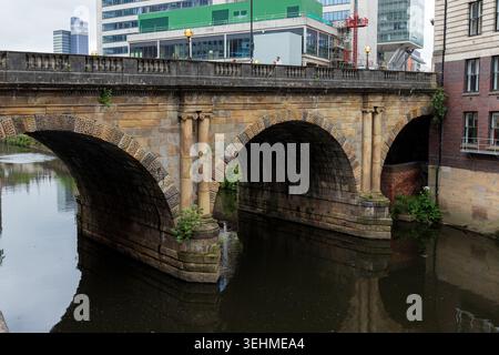 Il Blackfriars Bridge vittoriano con archi in pietra sul fiume Irwell a Deansgate, Manchester, con edifici contemporanei oltre. Foto Stock