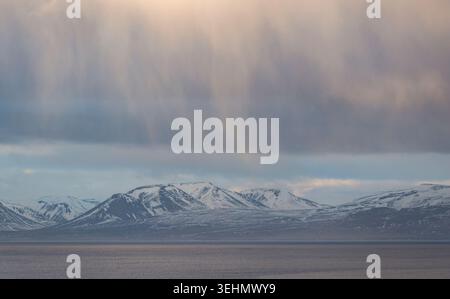 Montagne innevate vicino a Hvitserkur, Islanda, si innalzano sopra una tranquilla baia costiera in inverno, con nebbie morbide e nuvole spettacolari che creano una N tranquilla e tranquilla Foto Stock
