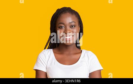 La donna sorridente si erge con sicurezza davanti allo sfondo giallo brillante indossando una camicia semplice Foto Stock