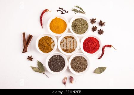 Vista dall'alto di spezie e semi assortiti in piccole ciotole su sfondo bianco, con pepe, curcuma, coriandolo, curry, lino, sesamo e chia, con Foto Stock