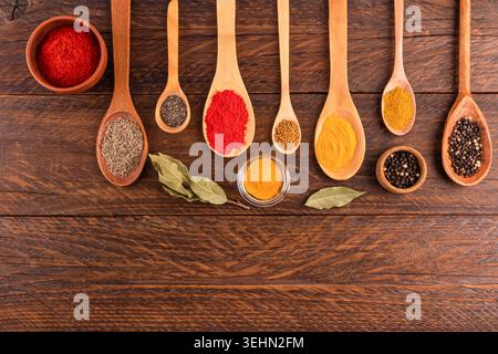 Colorato assortimento di spezie e semi in cucchiai di legno su tavola rustica, con pepe, curcuma, coriandolo, curry, lino, sesamo e chia per il coo Foto Stock