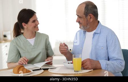L'accompagnatore fa colazione a un anziano al tavolo di legno all'interno Foto Stock