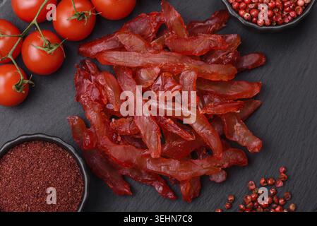 Cibo, fette di pollo essiccate, con gusto di ciliegia o prugna, sale e spezie su sfondo di cemento scuro Foto Stock