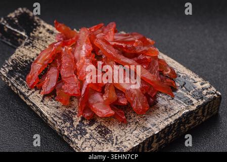 Cibo, fette di pollo essiccate, con gusto di ciliegia o prugna, sale e spezie su sfondo di cemento scuro Foto Stock