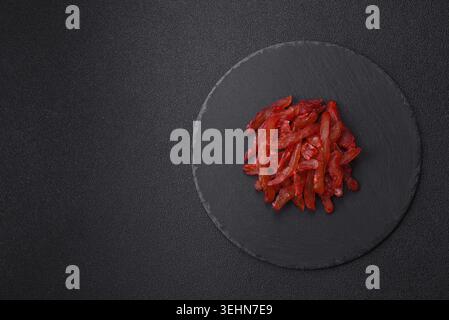 Cibo, fette di pollo essiccate, con gusto di ciliegia o prugna, sale e spezie su sfondo di cemento scuro Foto Stock