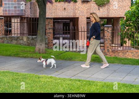 Donna bianca anziana che si gode una passeggiata con il suo piccolo cane in giro per la città Foto Stock