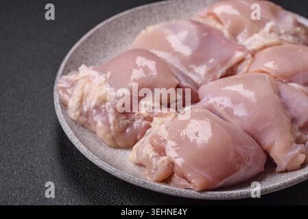 Cibo, filetti di coscia di pollo crudi freschi con sale, spezie ed erbe aromatiche su sfondo di cemento scuro Foto Stock