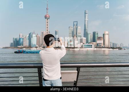 Vista posteriore dell'uomo asiatico che utilizza lo smartphone per fotografare la Oriental Pearl Tower e lo skyline di Shanghai dal punto panoramico del Bund in Cina Foto Stock