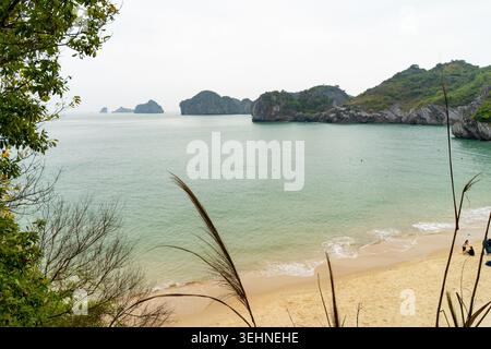 Una tranquilla spiaggia tropicale con calme acque turchesi e lussureggianti isole carsiche verdi in lontananza, che offrono una fuga tranquilla Foto Stock
