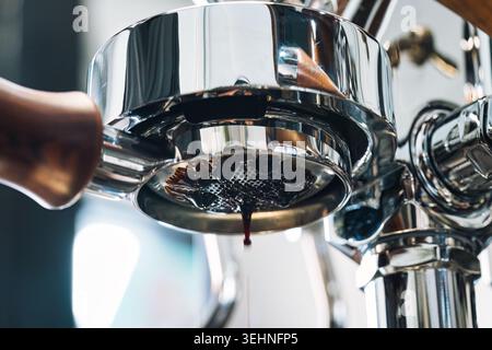 Macchina per caffè espresso da vicino con caffè tostato scuro con crema di zecche che fluisce dal portafiltro senza fondo in un ambiente da caffè moderno Foto Stock