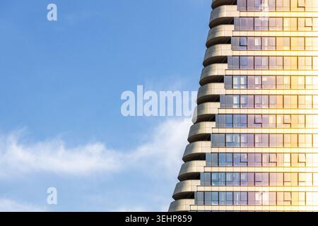 Vista ad angolo basso della moderna facciata del grattacielo con balconi curvi contro il cielo blu al tramonto. Futuristica architettura aziendale in vetro con poliziotto Foto Stock