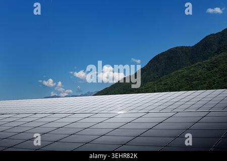 Pannelli solari fotovoltaici in un paesaggio naturale con cielo blu, nuvole bianche e montagne verdi. Energia rinnovabile pulita, energia elettrica sostenibile Foto Stock