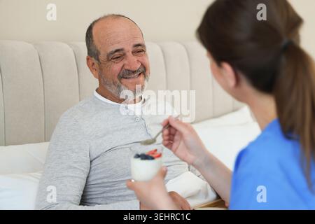 Assistente che fa colazione a un anziano a letto a casa Foto Stock