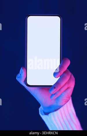 Smartphone femmina con presa a mano con schermo vuoto nelle luci al neon Foto Stock