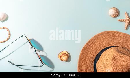 Accessori da spiaggia estivi con cappello di paglia, occhiali da sole, conchiglie e stelle marine disposti su sfondo blu pastello. Vacanza tropicale e concetto di viaggio. Foto Stock