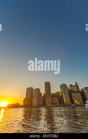 Una vista grandangolare del Lower Manhattan Financial District al tramonto, caratterizzato da alti edifici che brillano con luce dorata e riflessi del sole Foto Stock