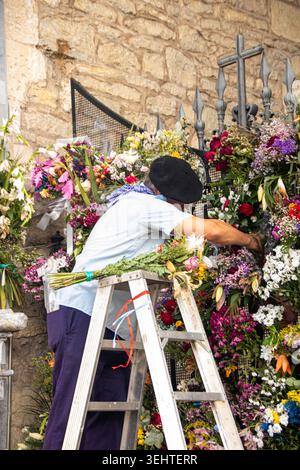 VITORIA-GASTEIZ, SPAGNA - AGOSTO 2025: Un uomo locale che indossa un tradizionale abbigliamento festivo con un berretto nero (txapela) si erge su una scala per organizzare il bouque Foto Stock
