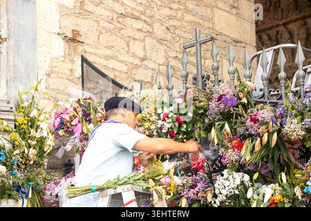 VITORIA-GASTEIZ, SPAGNA - AGOSTO 2025: Un uomo locale che indossa un tradizionale abbigliamento festivo con un berretto nero (txapela) si erge su una scala per organizzare il bouque Foto Stock