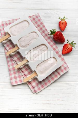 I papaveri di yogurt alla fragola vengono inseriti in una muffa su un tovagliolo a quadri con fragole fresche Foto Stock