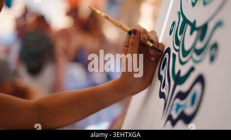 Mano dell'artista che tiene in mano il pennello, dipingendo calligrafia su tela Foto Stock
