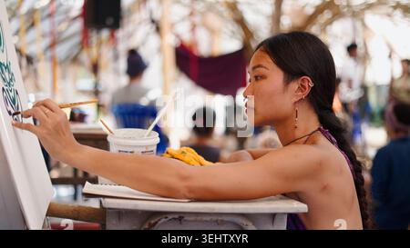 Artista donna che dipinge intensamente opere d'arte creative su tela in un festival all'aperto Foto Stock