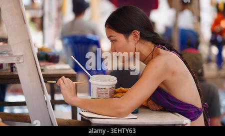 Giovane artista donna che si concentra, dipinge su tela con pennello durante il workshop all'aperto Foto Stock