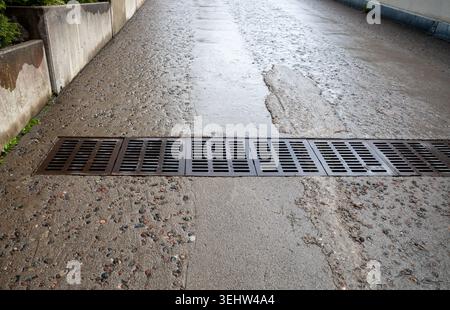 Griglia di drenaggio industriale su superfici stradali in calcestruzzo bagnato in ambienti urbani Foto Stock