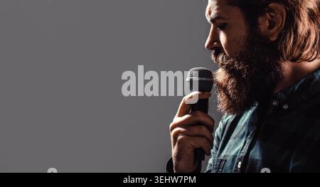 Microfono. L'uomo barbuto nel karaoke canta una canzone in un microfono. Un uomo frequenta il karaoke. Uomo barbuto che canta con il microfono. Copia spazio Foto Stock