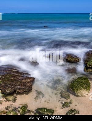Onde oceaniche sfocate in movimento che lavano rocce sulla spiaggia Foto Stock
