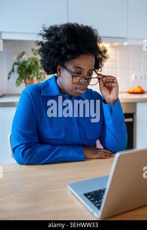 Una donna afroamericana stanca con gli occhi doloranti e stanchi guarda il laptop soffre di una visione sfocata, occhi secchi. Foto Stock