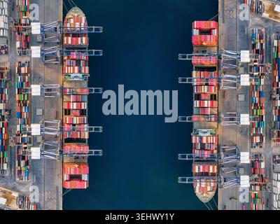 Vista aerea dall'alto di un grande terminal cargo con due navi super cargo attraccate e attività di scarico Foto Stock