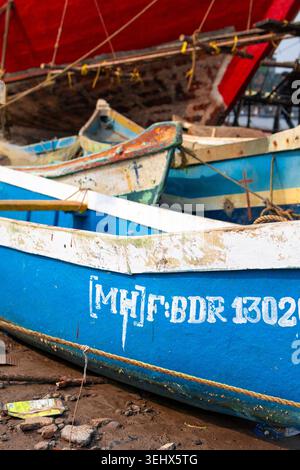 Primo piano di barche da pesca artigianali in legno blu con codici di registrazione e simboli a croce dipinti che poggiano su una riva fangosa, Maharashtra, India Foto Stock
